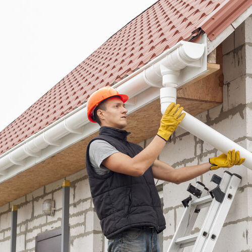 construction worker installs the gutter system on the roof