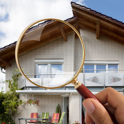 Person's Hand Holding Magnifying Glass Over Luxury House 