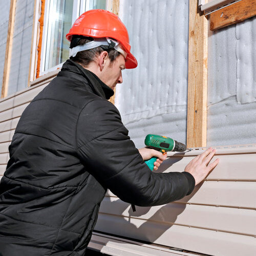 A worker installs panels of beige siding on the facade of the house